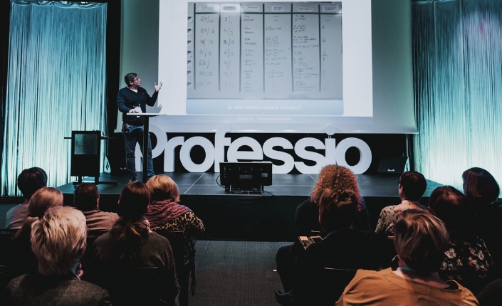 Kouluttaja, joka seisoo luokan edessä, osoittaa valkokangasta ja kouluttaa kouluttautujia